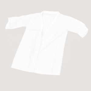 Bata blanca desechable con mangas, extendida sobre fondo gris claro, fabricada en tejido no tejido ligero, diseñada para tratamientos estéticos o de fisioterapia.