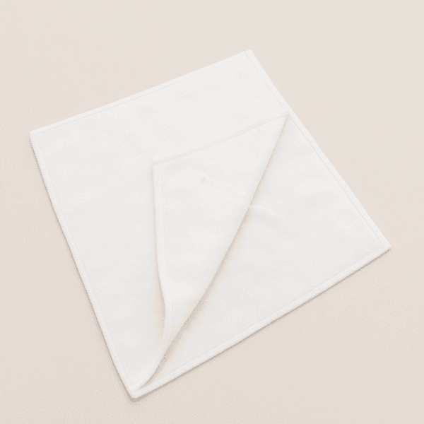 Toalla de microfibra blanca 40x75 cm doblada sobre superficie beige – ideal para uso profesional.