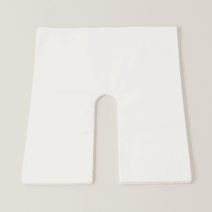 Cubierta desechable blanca con apertura en forma de herradura para reposacabezas de camilla, presentada doblada.
