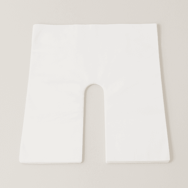 Cubierta desechable blanca con apertura en forma de herradura para reposacabezas de camilla, presentada doblada.